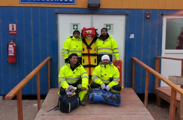 Equipo prehospitalario REST911 con camilla frente a un policlínico modular de faena