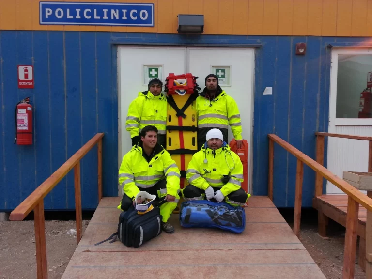 Equipo prehospitalario REST911 con camilla frente a un policlínico modular de faena