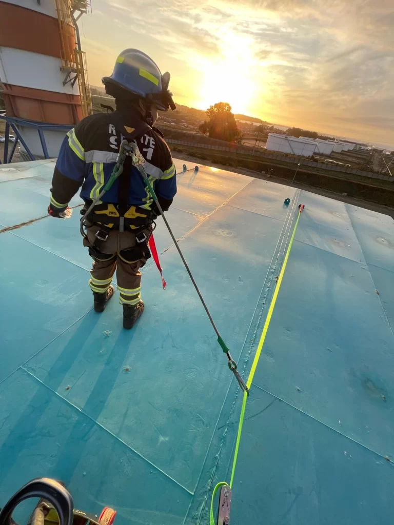Rescatista con línea de vida en techumbre industrial al atardecer